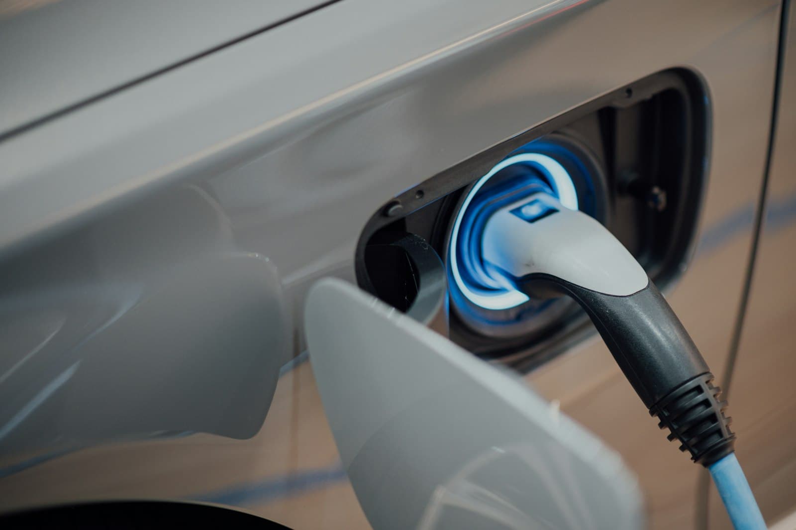 Electric vehicle charging connector plugged into a car with a blue glow