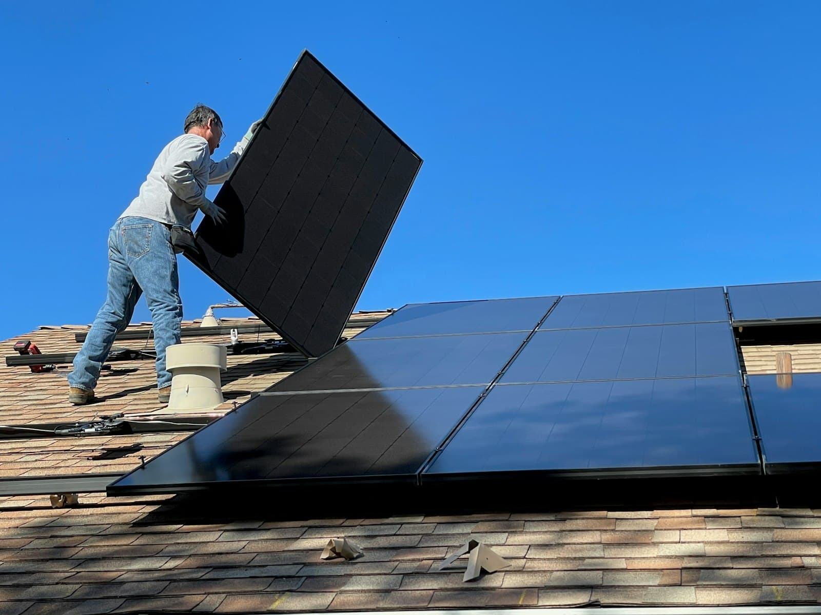 An installer carries a sleek black solar panel onto a rooftop against a deep blue sky
