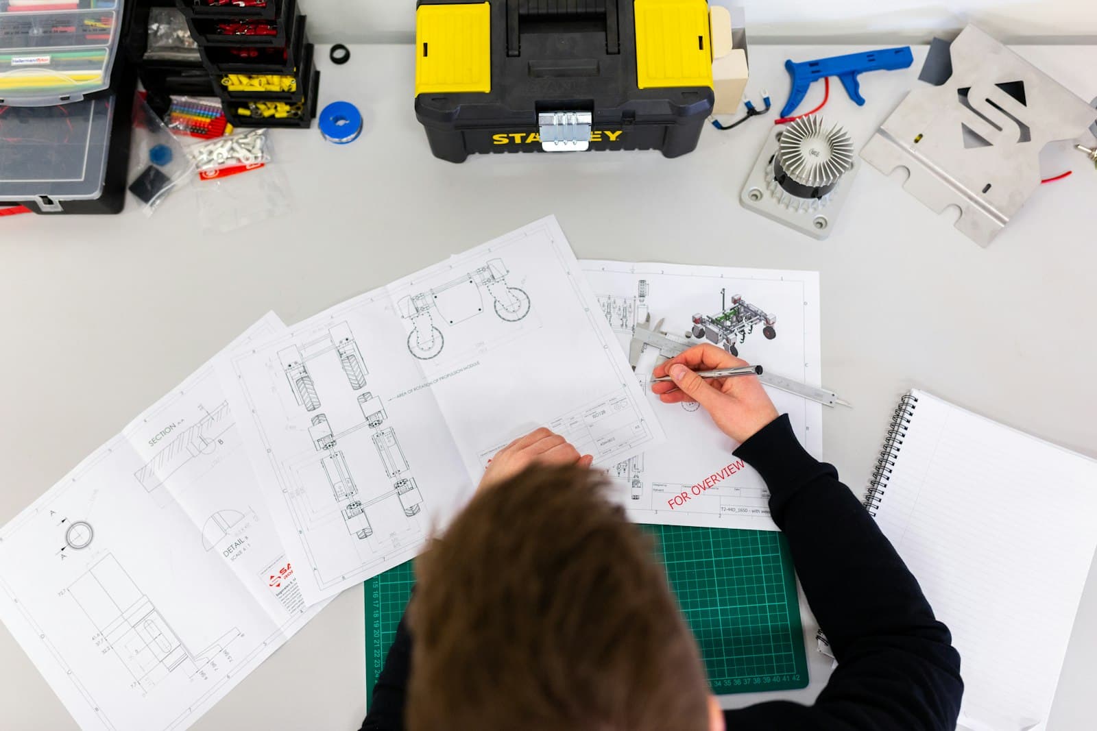 An engineer working over technical drawings and measuring instruments at a design desk